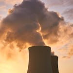 Cooling towers release smoke into a dramatic sunset sky, highlighting environmental impact.